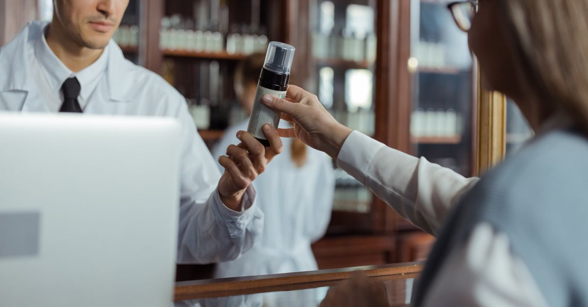A pharmacist in a white uniform hands medication to a customer across the counter. — 24 hour pharmacy