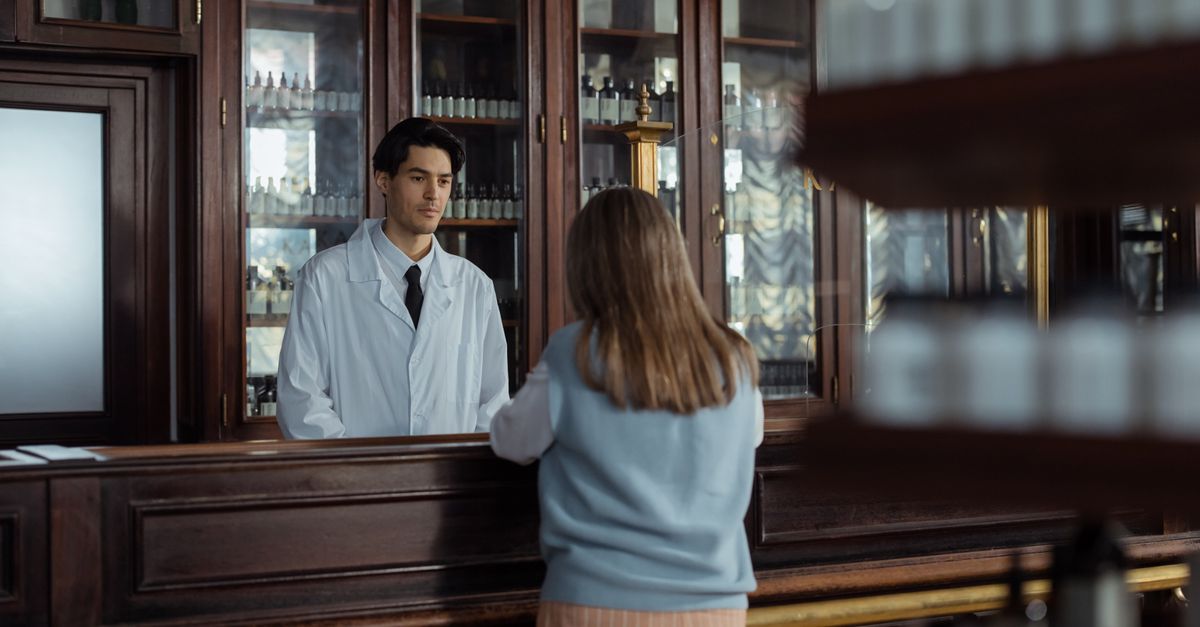 A pharmacist assists a customer at a vintage wooden pharmacy counter indoors. — safeway pharmacy