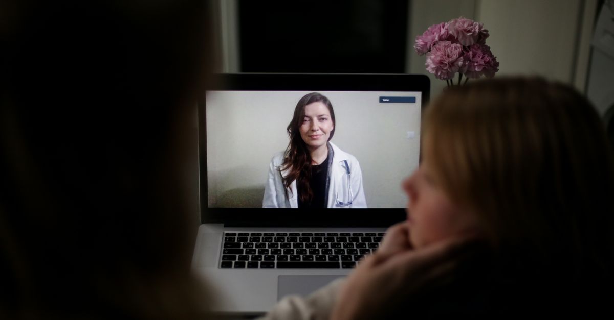 A doctor appears on a laptop screen during an online medical consultation at home. — primary care