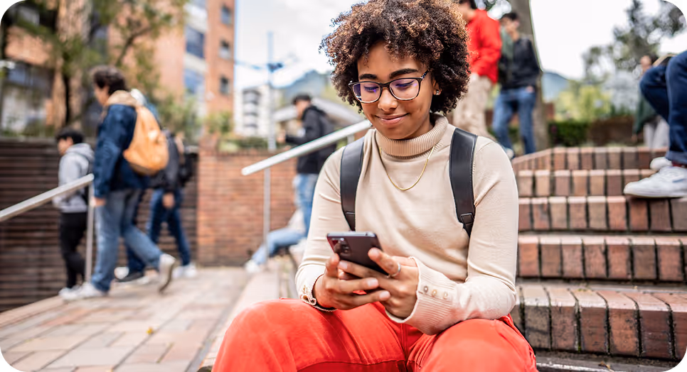 Student checking phone on outdoor brick steps with backpack