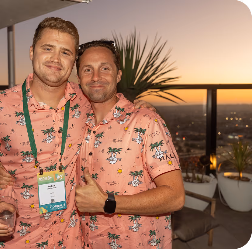 Two men in matching pink tropical shirts at sunset conference event