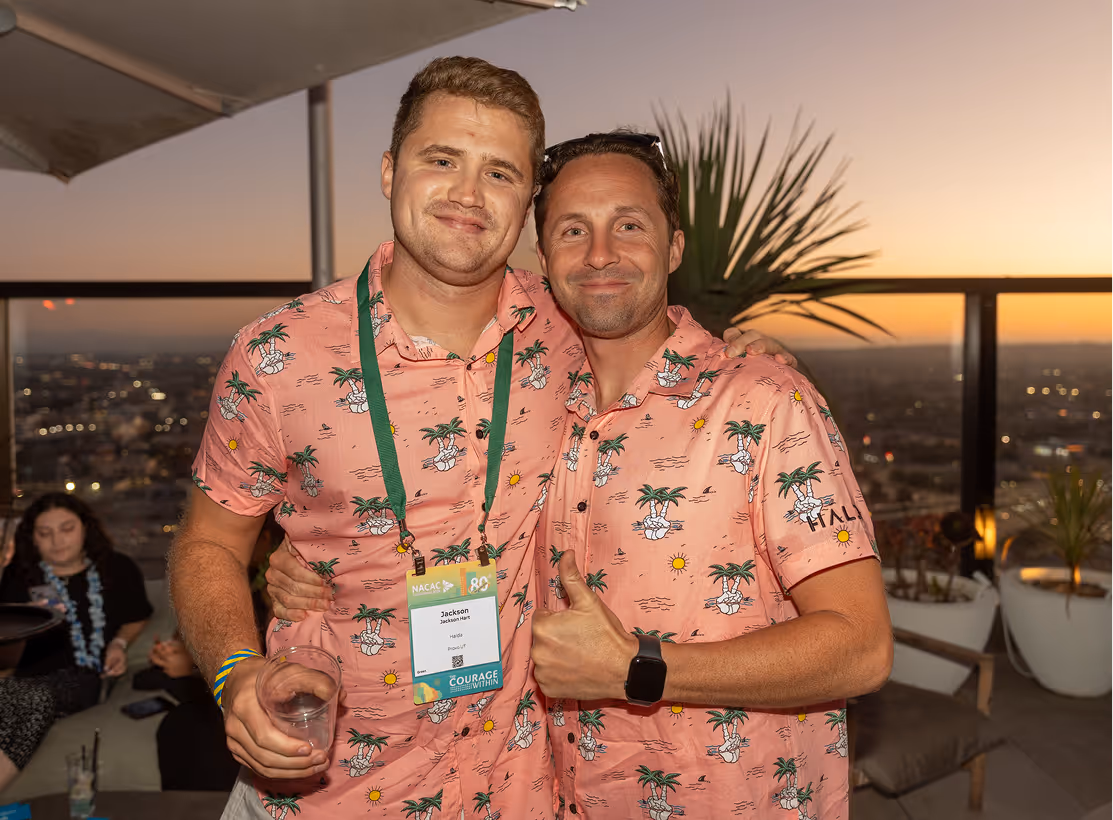 Two men in matching pink tropical shirts at conference event with sunset view