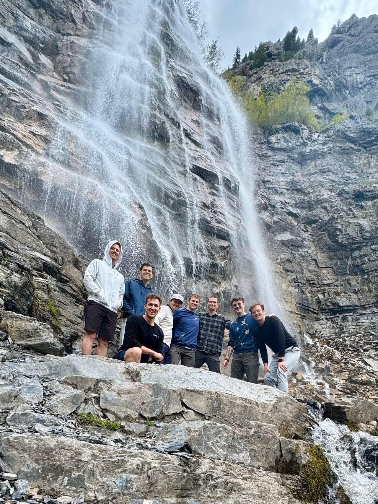 Group of men posing together near massive waterfall in rocky mountain landscape