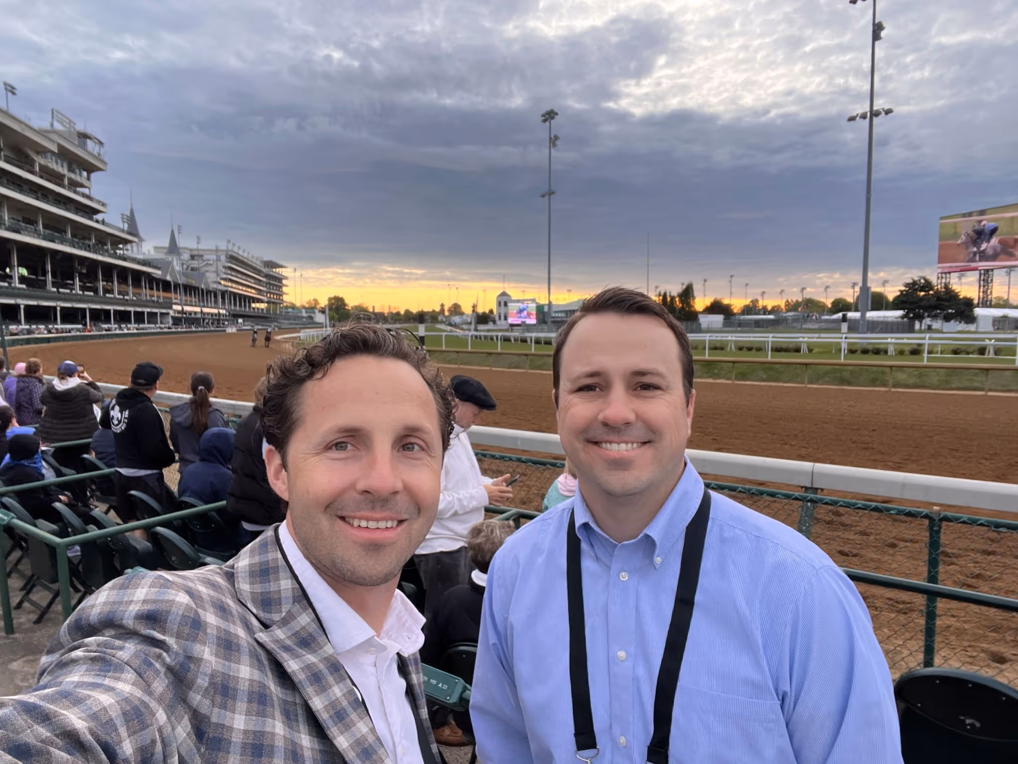 Two men smiling at horse racing track during sunset