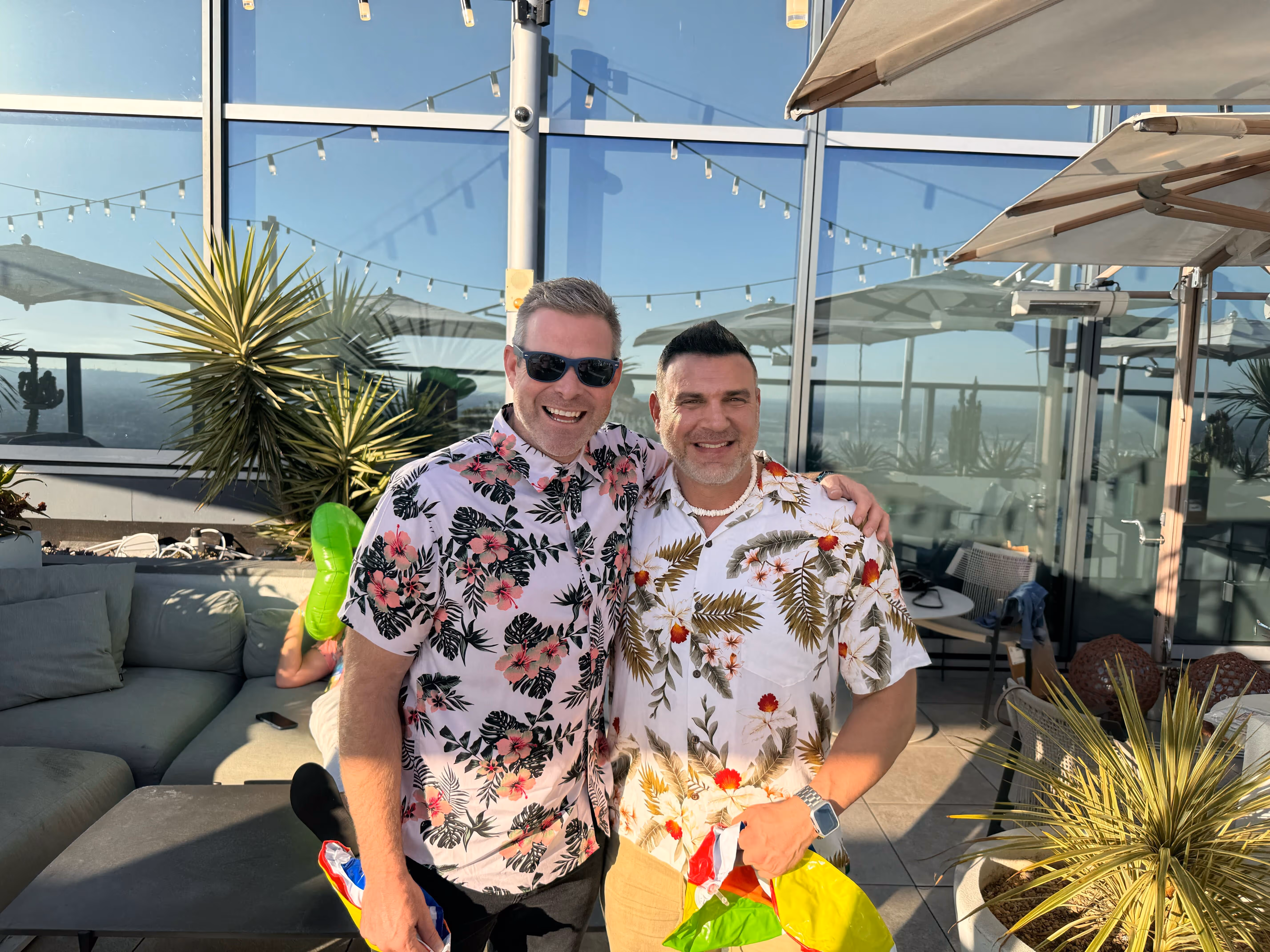 Two men in Hawaiian shirts smiling together on a rooftop terrace