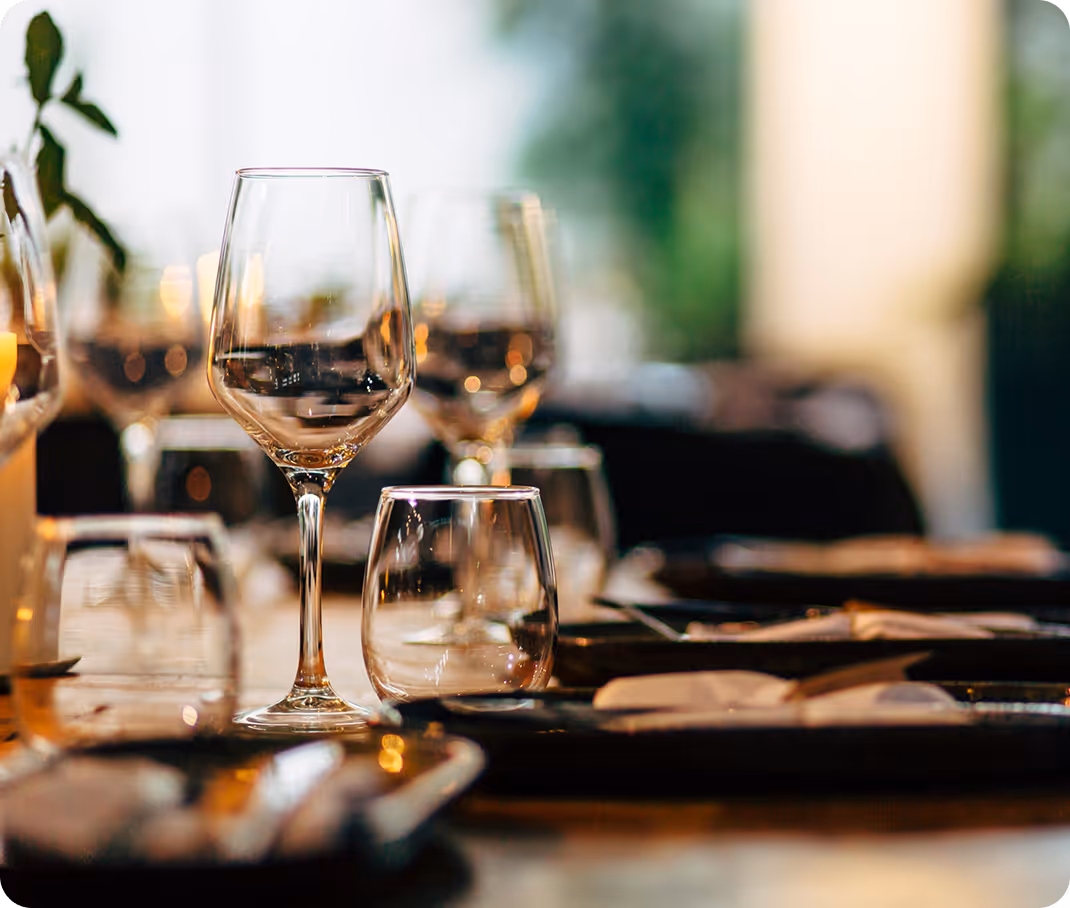 A smiling family gathered around a laptop at a table. A father and young son sit together, looking at the screen, while the mother stands beside them, watching and smiling. A mug and some papers are on the table.