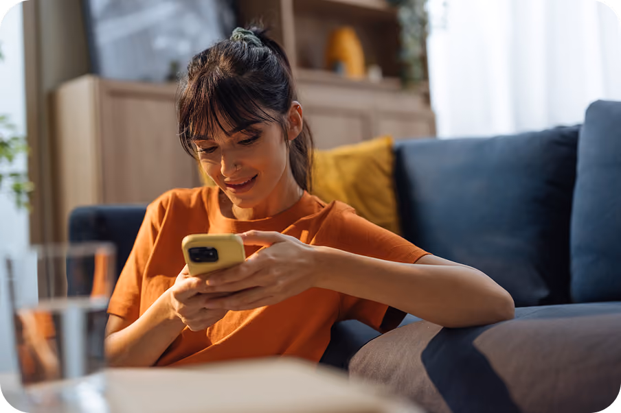 A prospective student smiling at her phone while sitting on a sofa at home