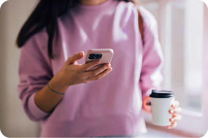 A student holding a phone and a coffee cup