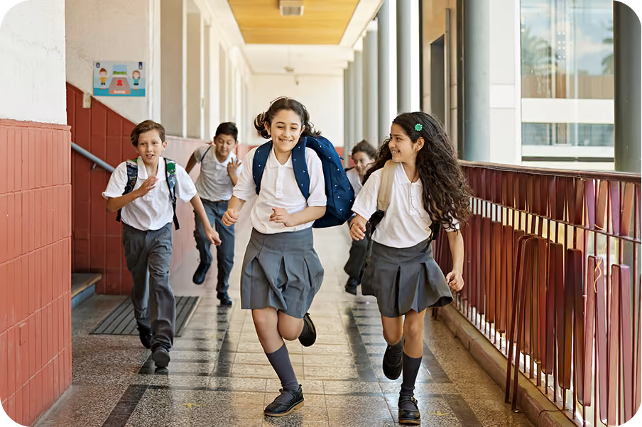 School pupils in uniform running and laughing along an outdoor school corridor