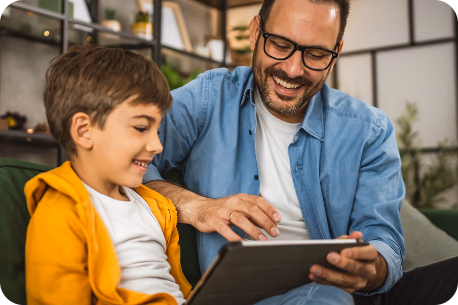 A father and his young son looking at a tablet together on a sofa