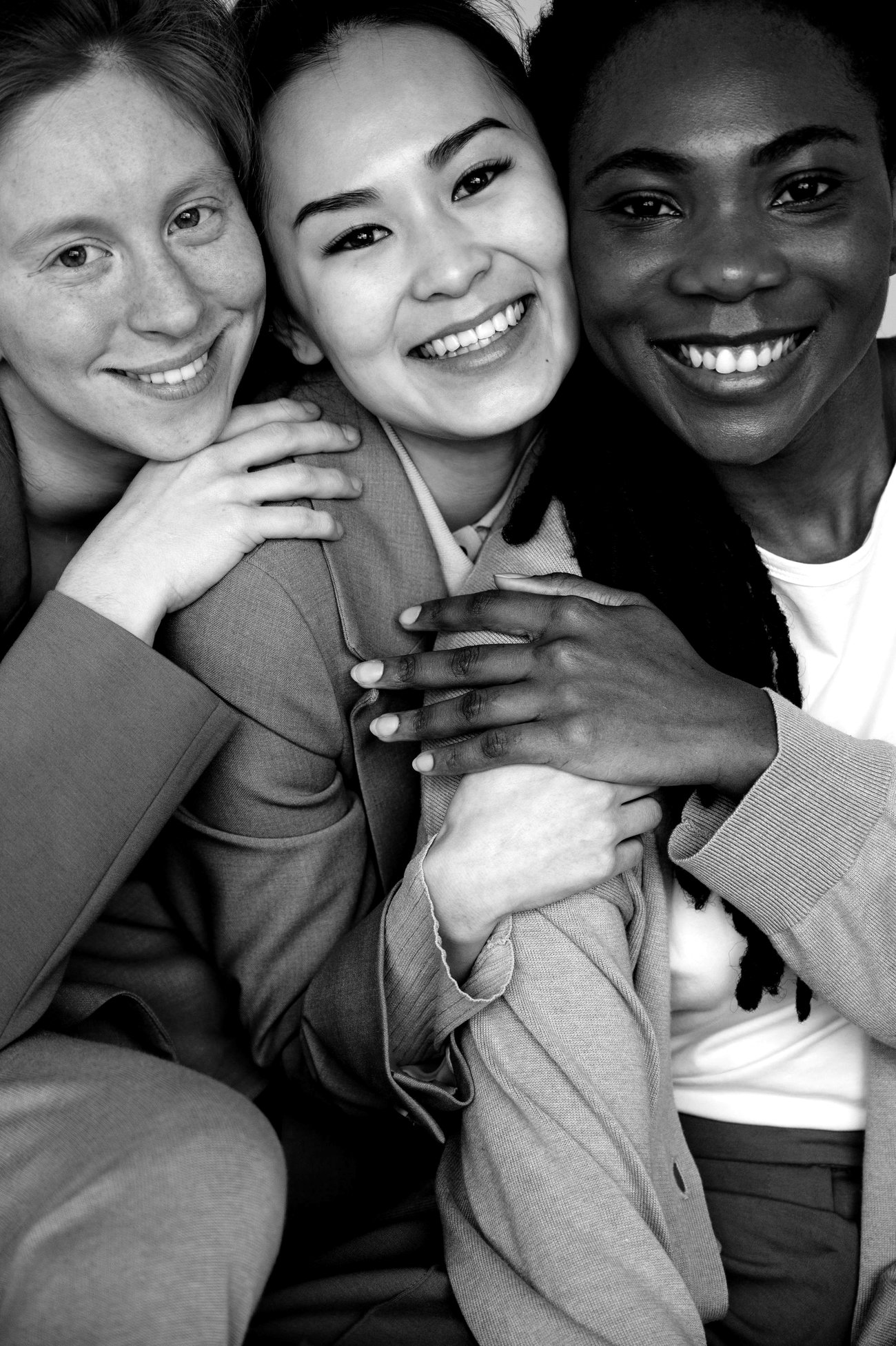 Three women holding each other and smiling, photographed in black and white