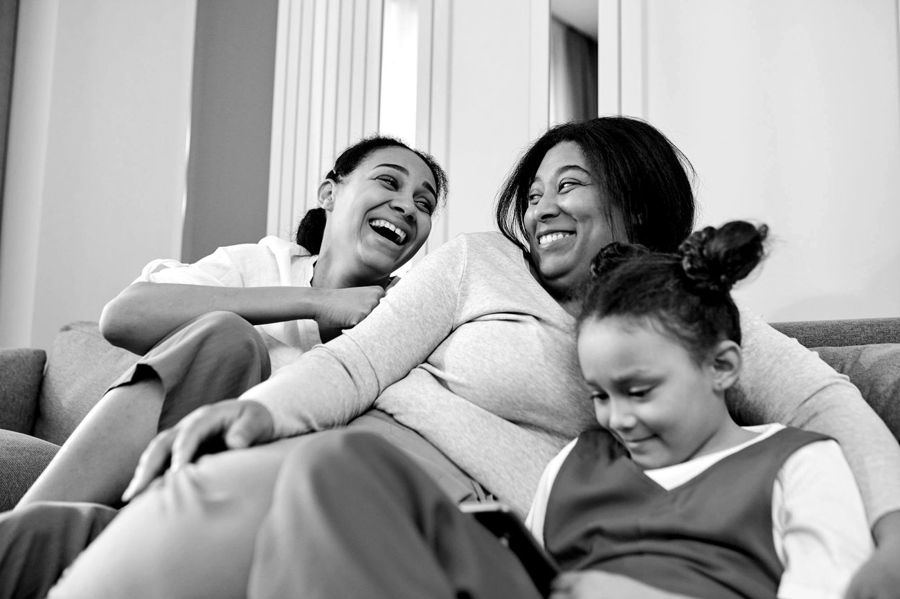 Women and a child laughing together at home, photographed in black and white