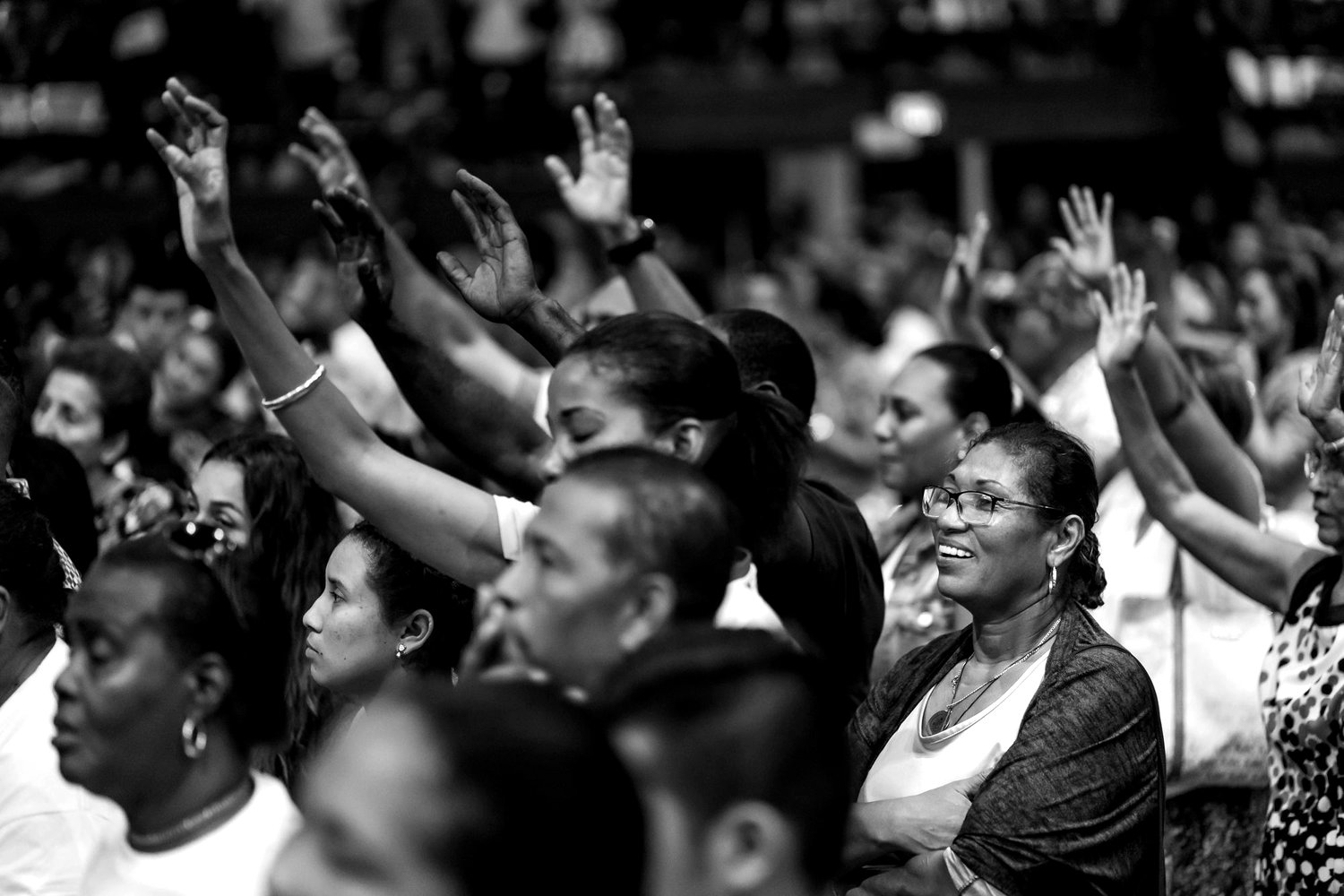 A congregation standing with hands raised together, photographed in black and white