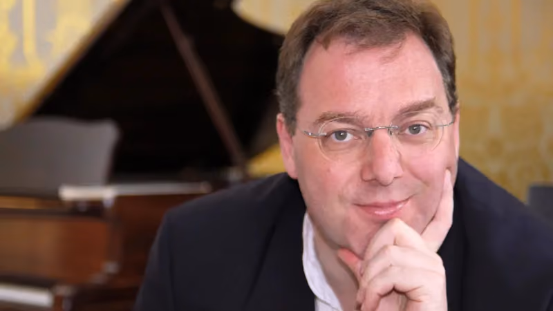 Mann lächelt mit Klavier im Hintergrund