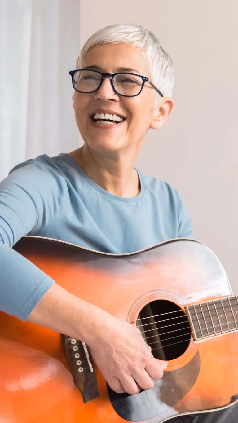 Ältere Frau lacht und hält Gitarre in der Hand