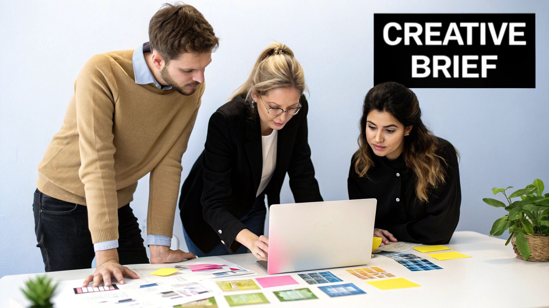 Three colleagues collaborating on a creative brief, reviewing designs and ideas on a table with a laptop.
