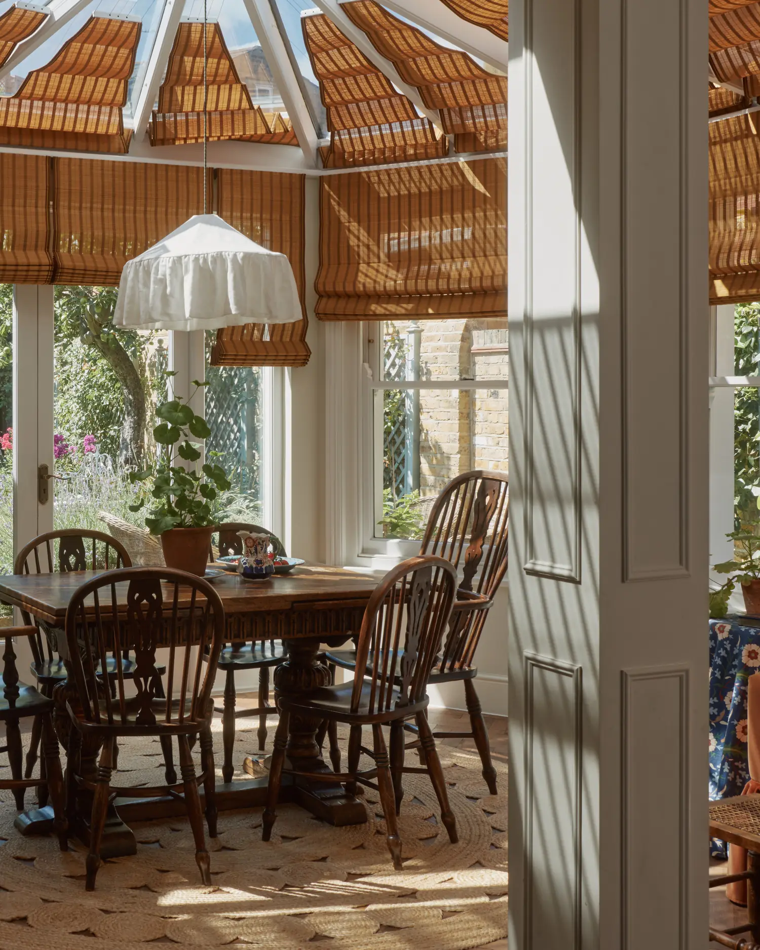 View through the doorway into the garden room, bamboo Roman blinds filtering light over the dining table