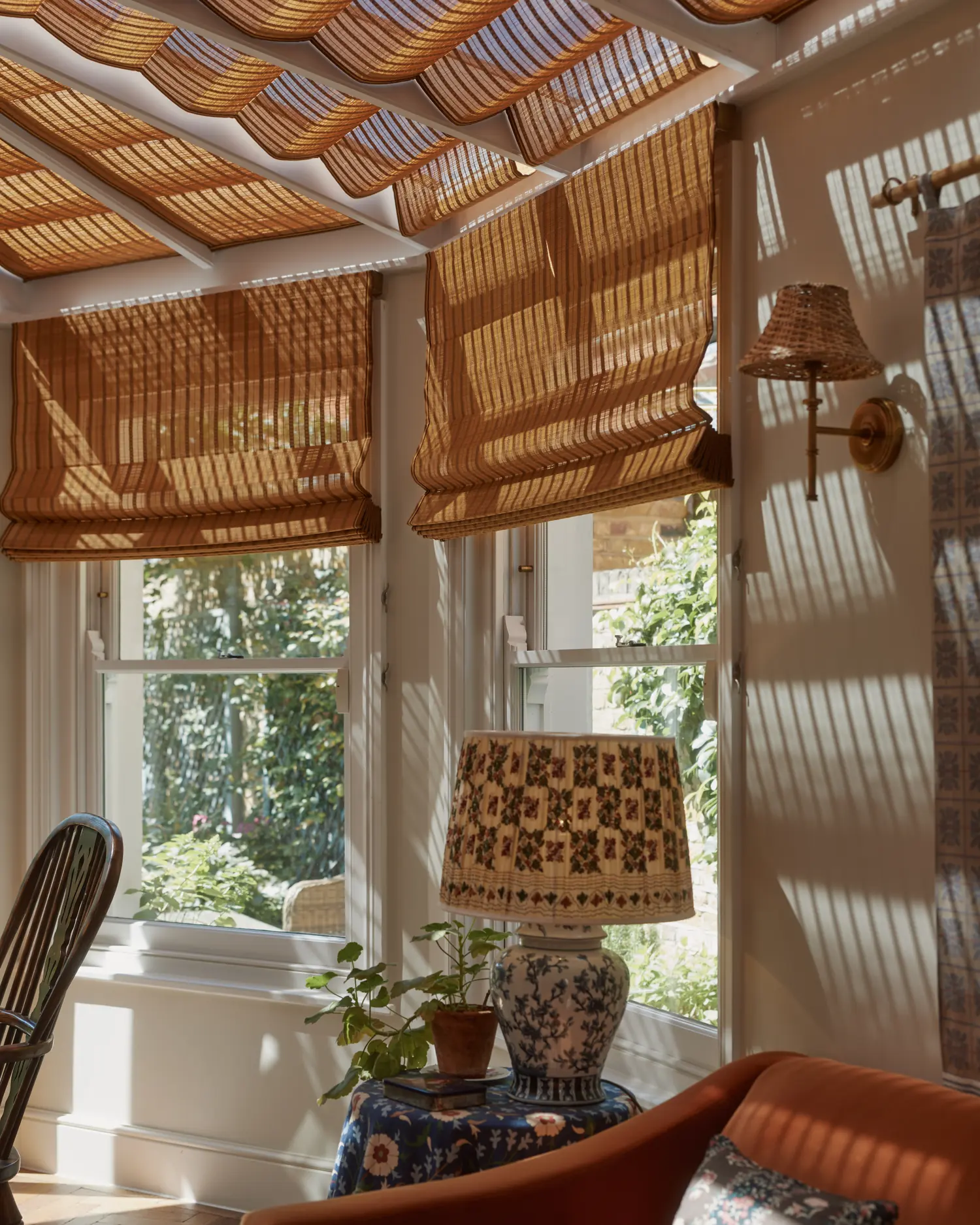 Corner of the garden room with bamboo blinds, a brass wall light and orange velvet sofa