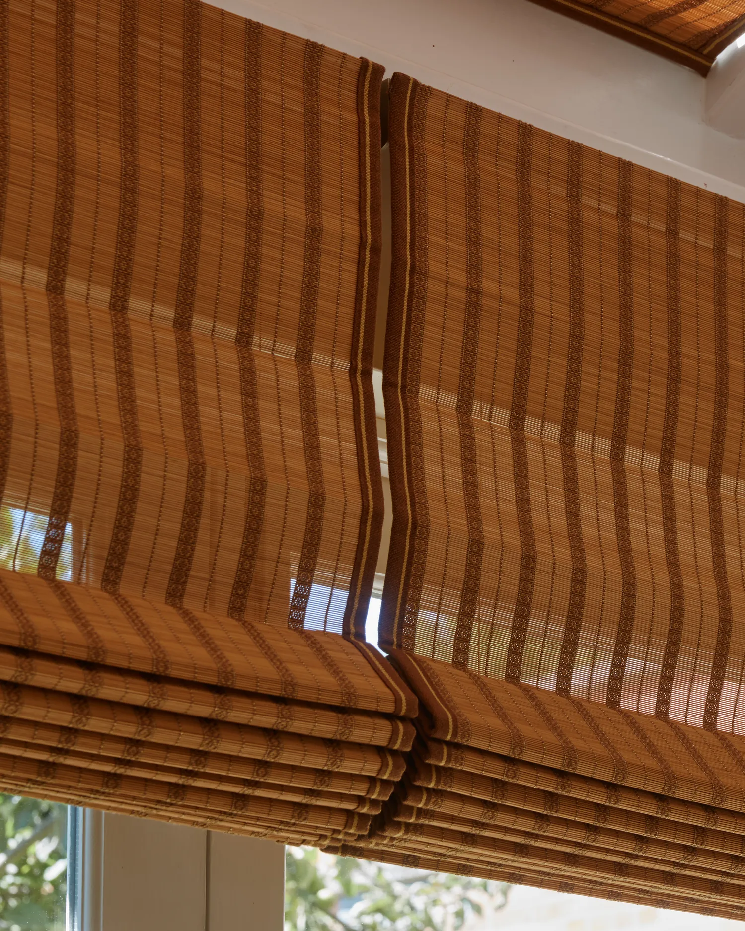 Detail of a bamboo Roman blind's folds at the window, greenery beyond the glass