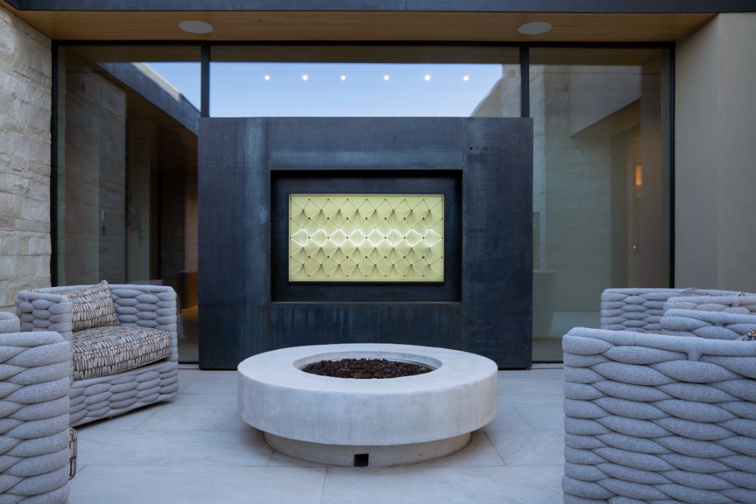 Outdoor patio with fire pit and framed art-mode TV on a stone wall