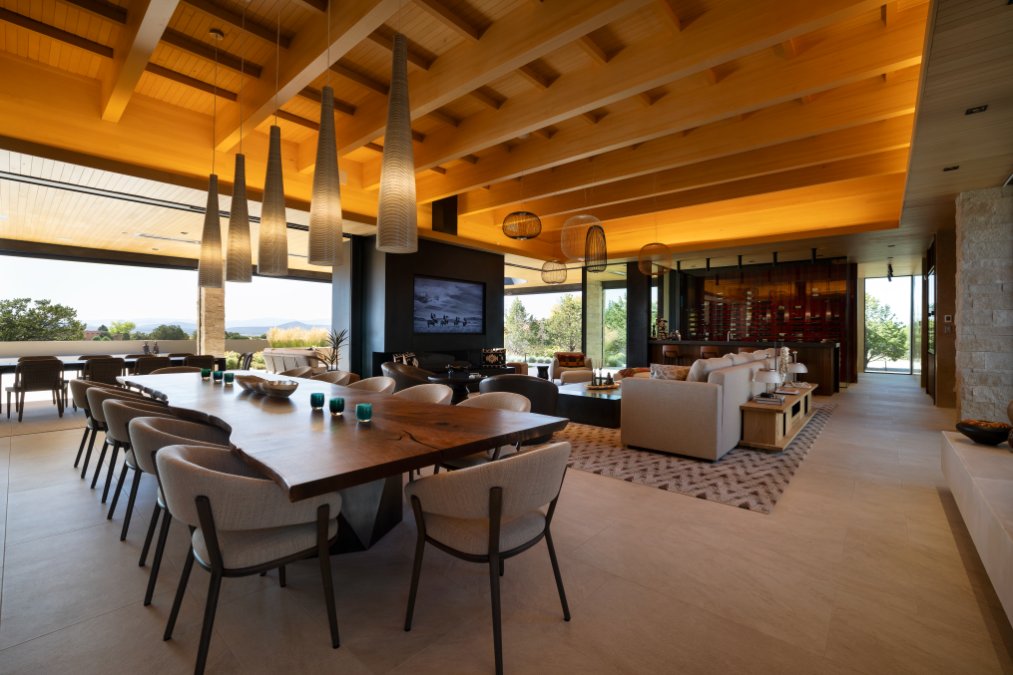 Great room with long dining table, lounge seating and integrated TV under a wood-beam ceiling