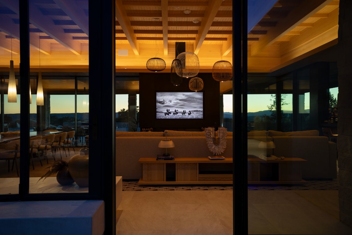 Living room with wall-mounted TV seen through glass doors at sunset
