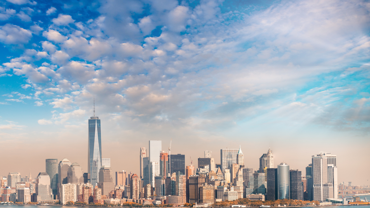 New York City skyline with One World Trade Center prominently visible under a partly cloudy blue sky.