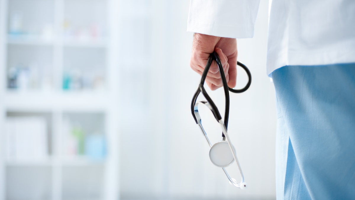 Close-up of a doctor holding a stethoscope with a blurred medical cabinet in the background.