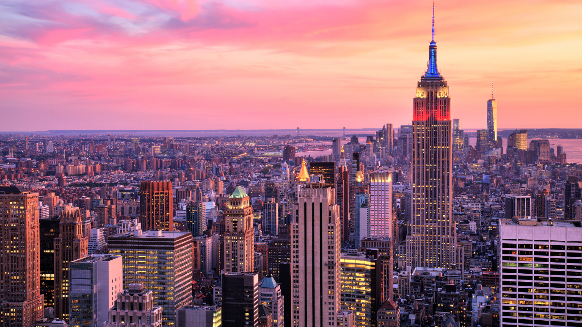 New York City skyline at sunset with the Empire State Building lit in red, white, and blue.