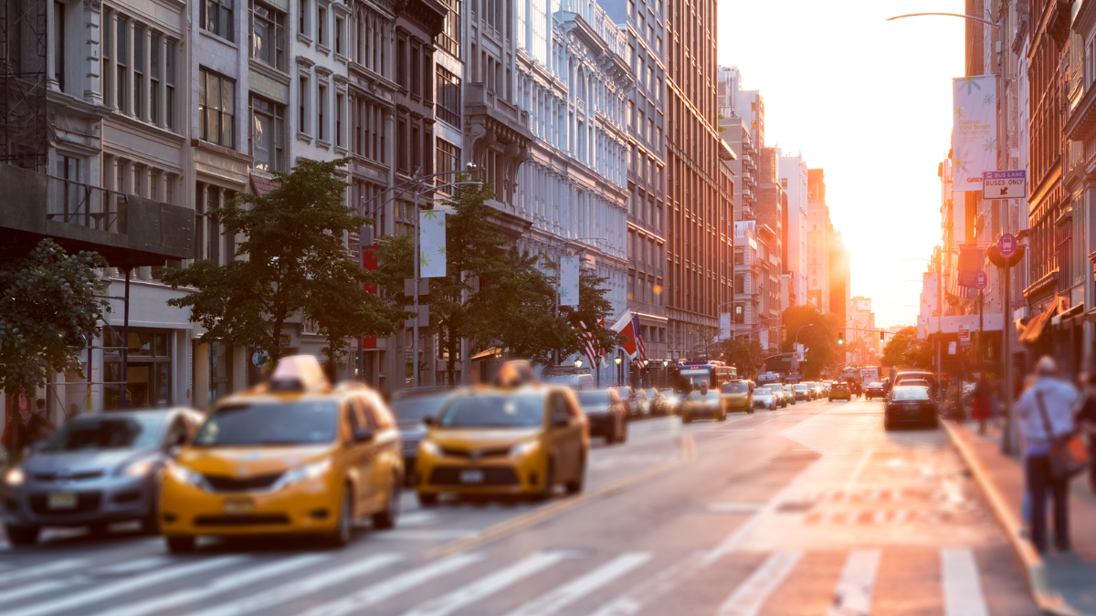 Sunset over busy city street with yellow taxis and tall buildings lining both sides.