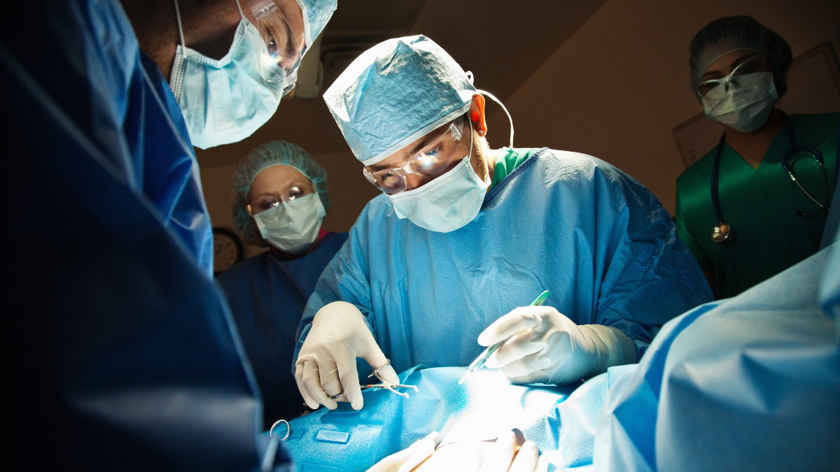 Surgeons wearing masks and gloves performing surgery in an operating room under bright light.