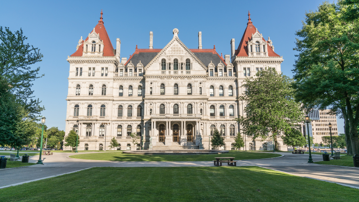 Front view of a large historic building in Albany New York with red steep roofs and manicured lawn in the foreground.