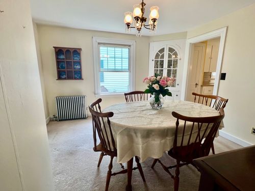 View of the dining room showing the table, facing towards the window and kitchen, radiator and decorative china holder.
