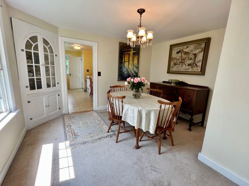 Carpeted dining room with a vintage built in shelving unit for plates. A window lights up the room.