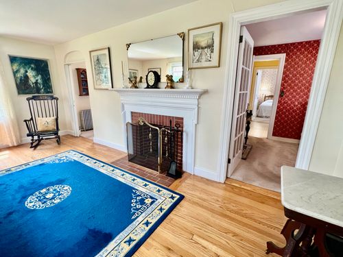 View of the living room fireplace looking towards the bedroom and dining room. Brick fireplace is framed by carved wood painted white.