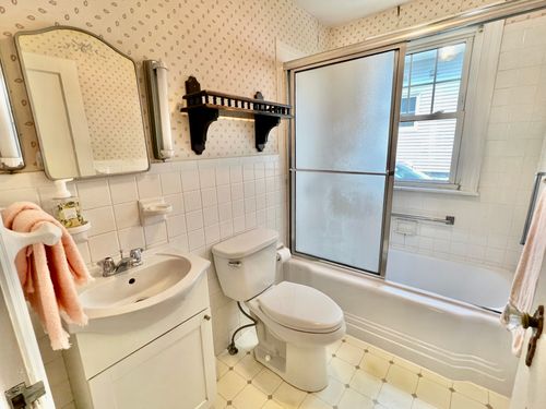 A bathroom with a sink, sliding door shower/bathtub, window, wood shelf, tile and wallpaper.