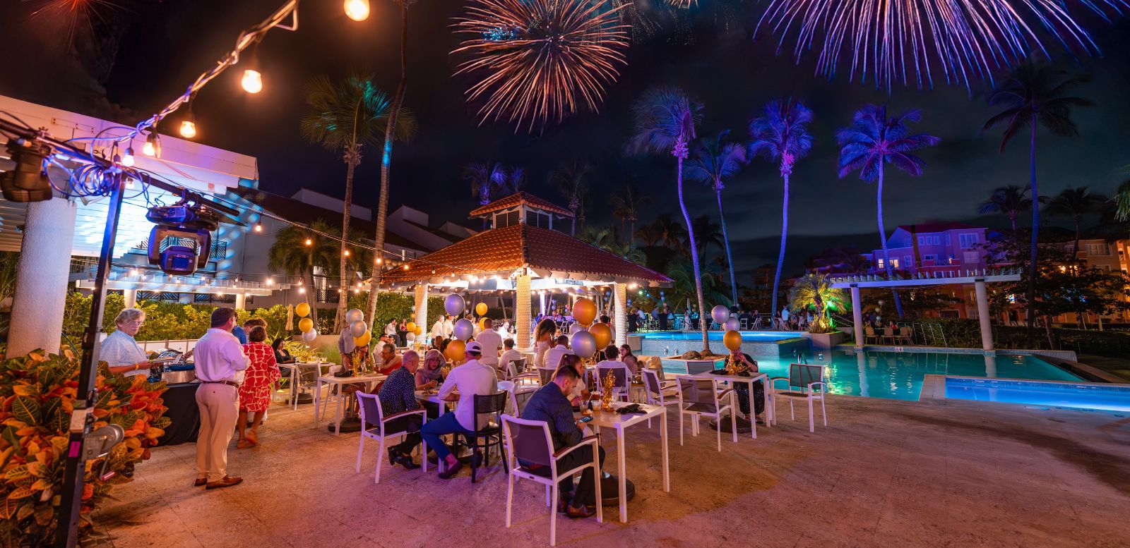 A beautiful view of fireworks above Costa infinity pool with people lounging around the bar.