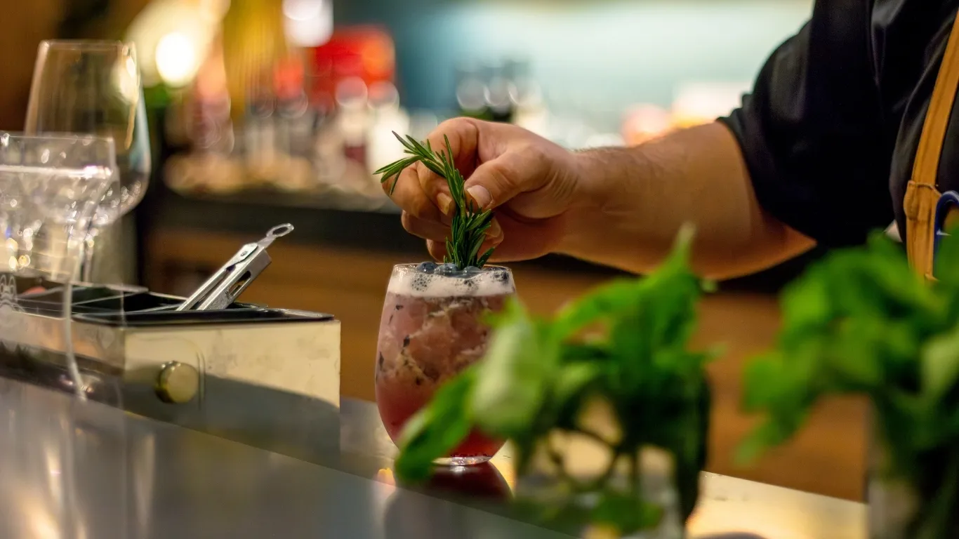 A bartender is placing greens on a mocktail as the finishing decorative touch. 