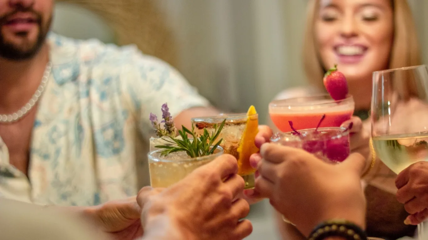 A group of four friends are toasting with drinks ranging from frozen cocktails to wine in a celebratory cheer.