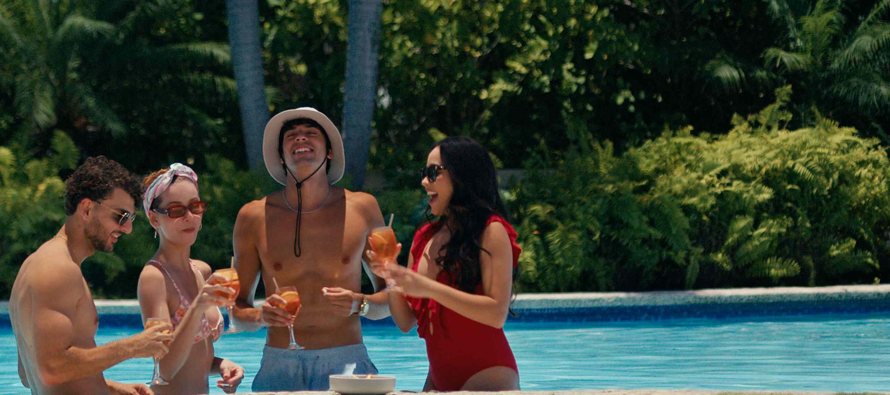 Four friends laughing and toasting with cocktails while standing in a resort pool.
