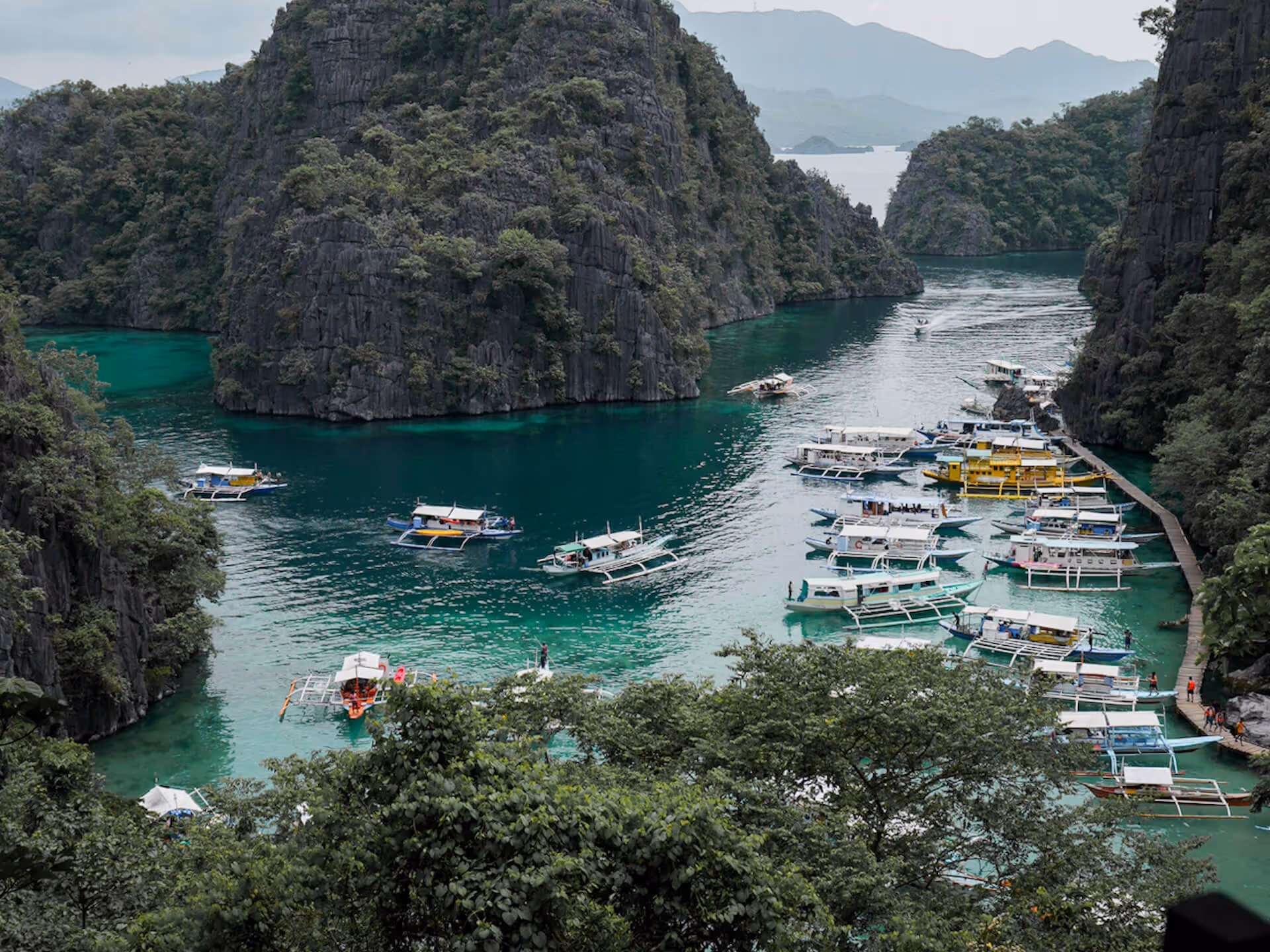 Boats docked and floating on turquoise water among towering forested limestone cliffs.