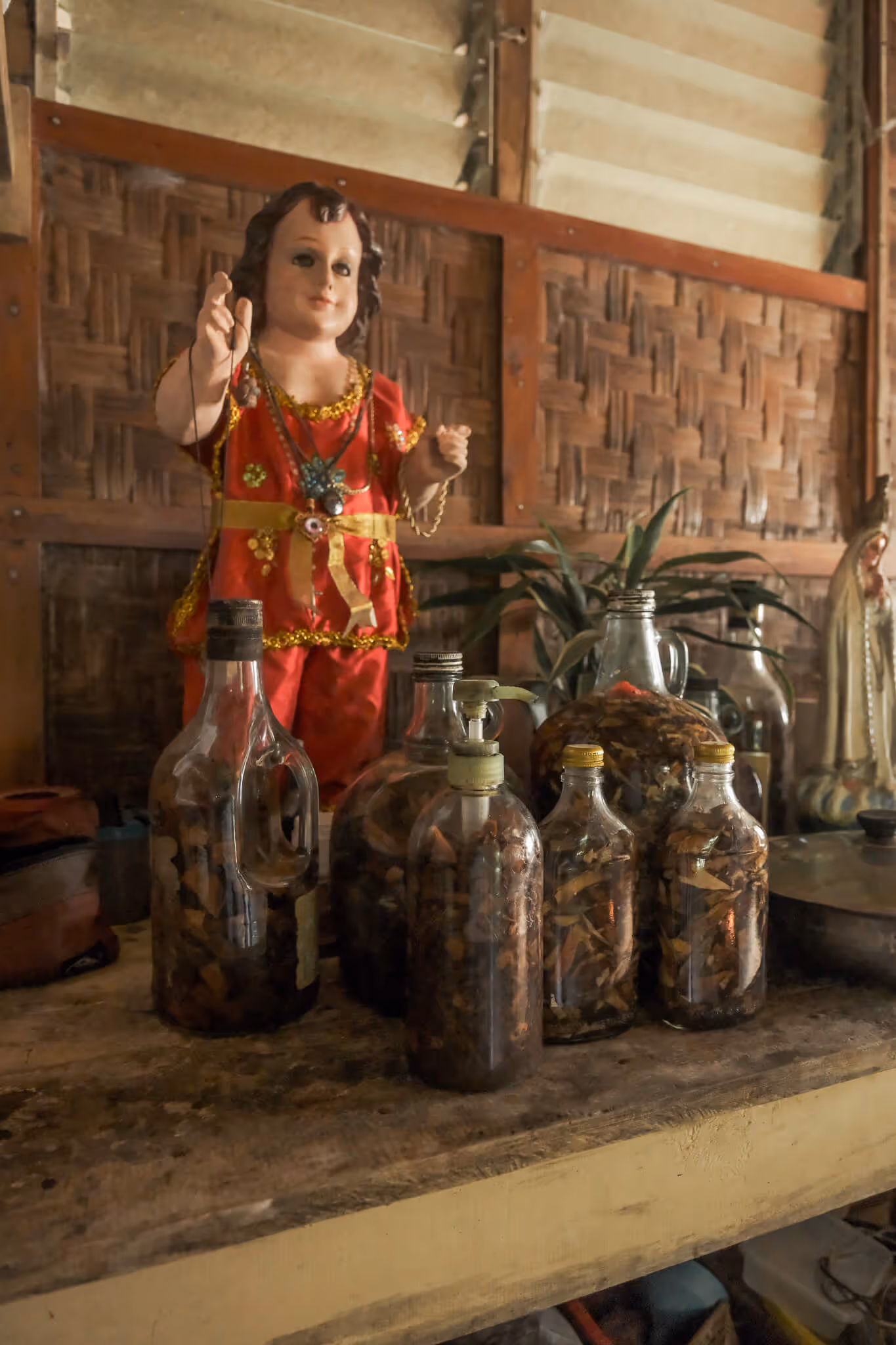 Small statue of a child in red clothes on a table with several glass jars filled with dried leaves.