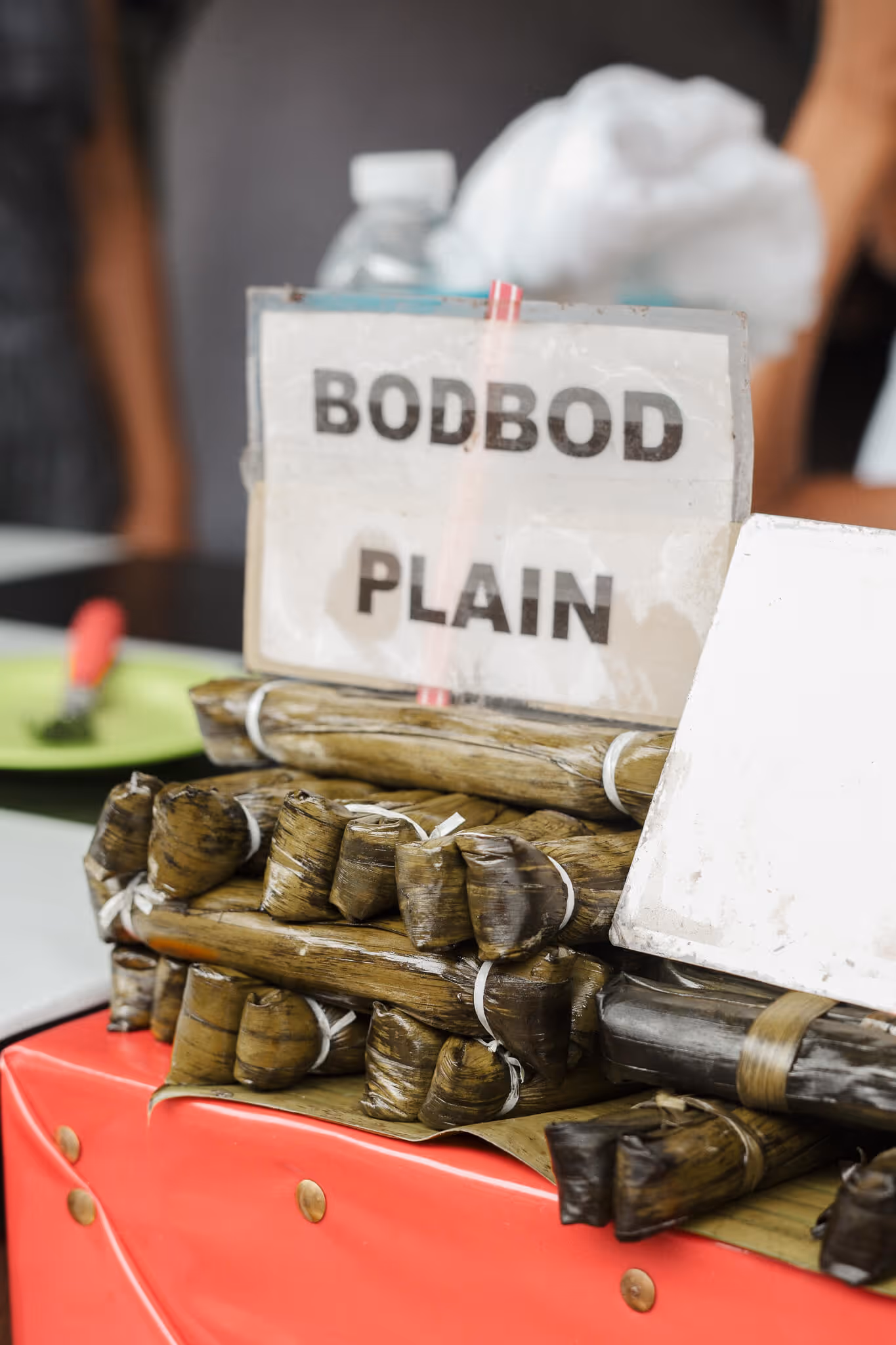 Stacks of traditional Filipino sticky rice cakes called Bodbod wrapped in banana leaves on a red table.