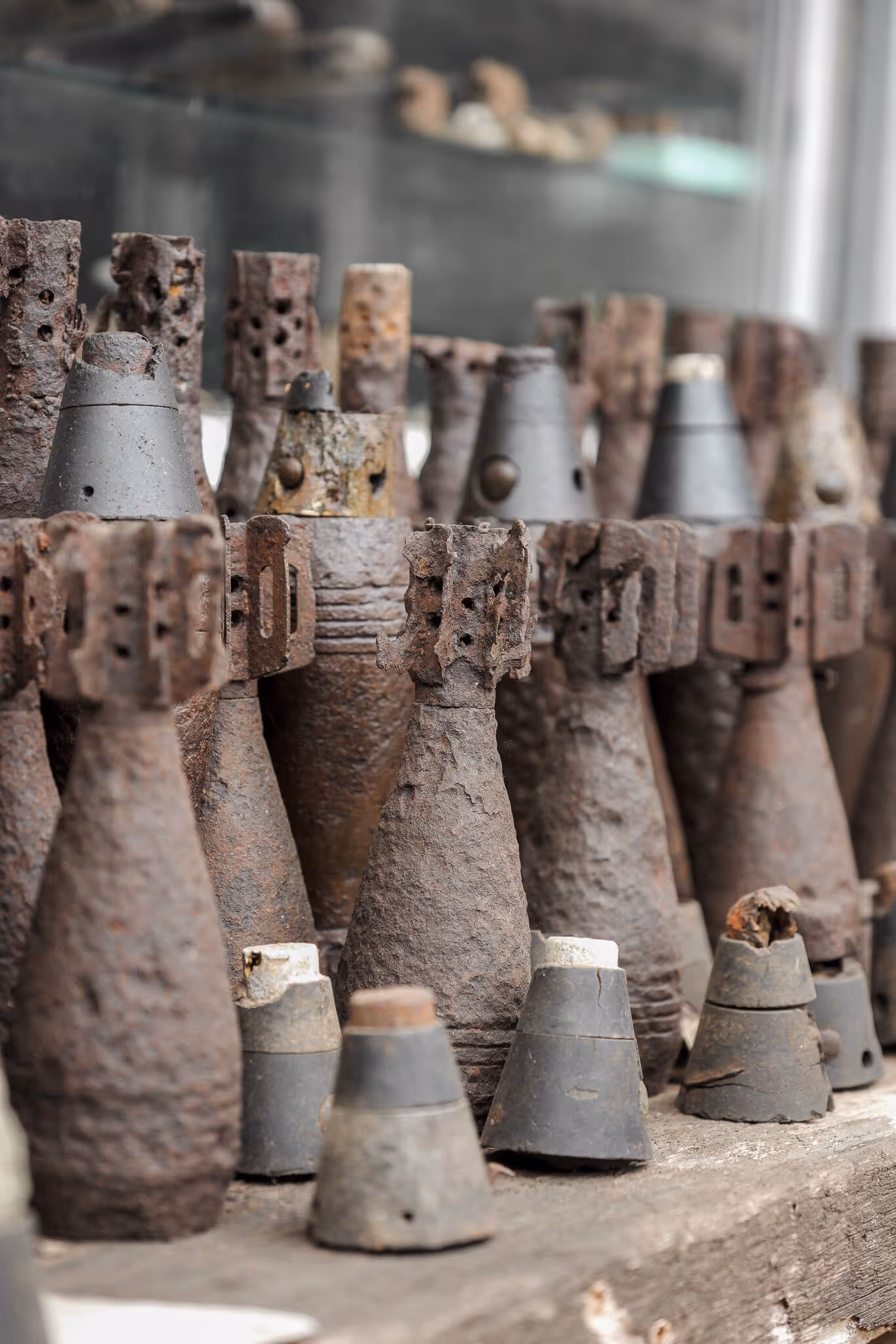 Rusty old mortars and artillery shells displayed on a wooden shelf.