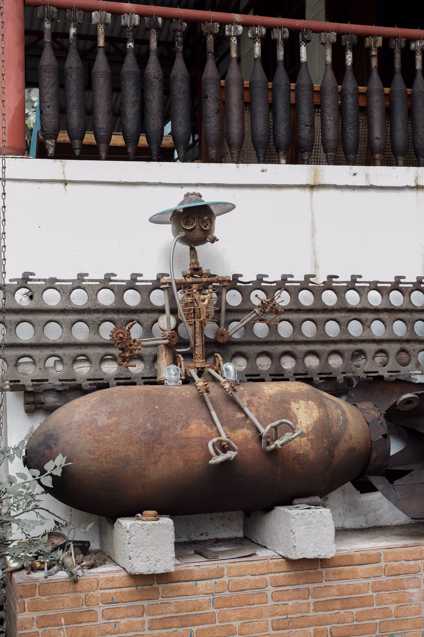 Rusty metal sculpture of a figure with a hat sitting on a large rusted bomb casing.