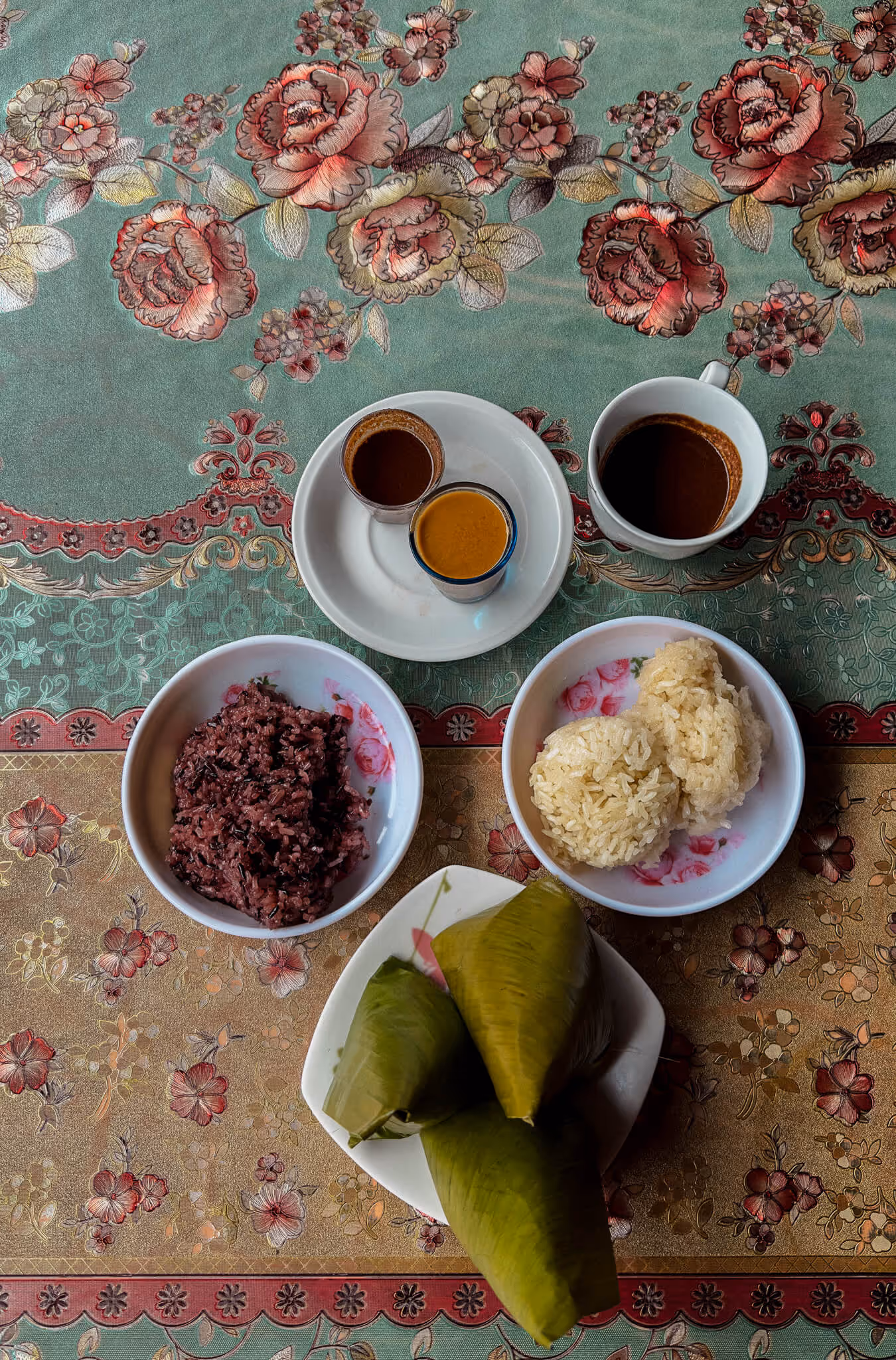 Traditional Filipino sticky rice treats with coffee cups on a floral patterned tablecloth.