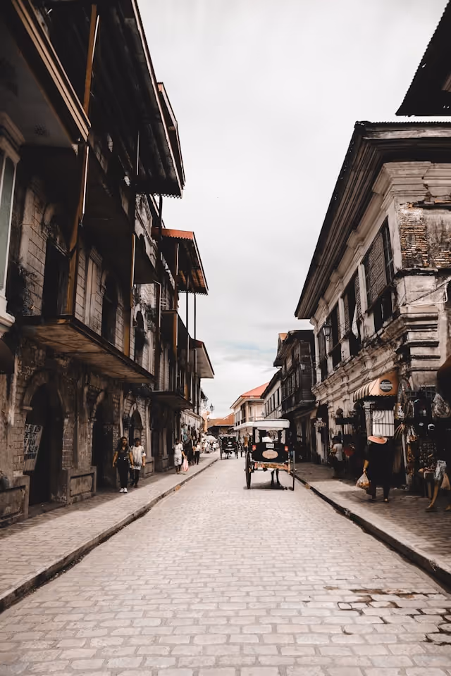 Cobblestone street lined with old colonial buildings and pedestrians, with a horse-drawn carriage in the center.