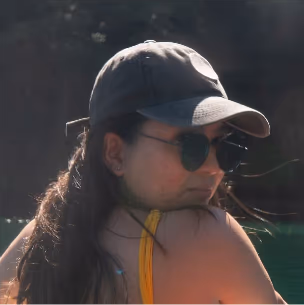 Woman wearing sunglasses and a cap looking over her shoulder near water.