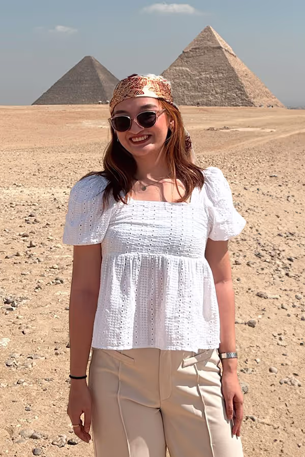 Woman in sunglasses and white blouse smiling in front of the Egyptian pyramids in a desert.