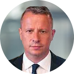 Headshot of a man with short hair wearing a suit and tie against a blurred background.